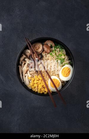 Ramen. Tagliatelle di Soba con uova, funghi shiitake e verdure, sparate dall'alto su uno sfondo scuro con bastoncini e copia Foto Stock