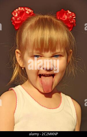 La bambina mostra la lingua. Ritratto di bambino sorridente che mostra la sua lingua in divertenti archi rossi. Infanzia Foto Stock