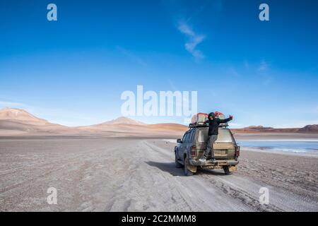 giovane uomo marrone che si trova sulle spalle di un suv nel deserto della bolivia Foto Stock