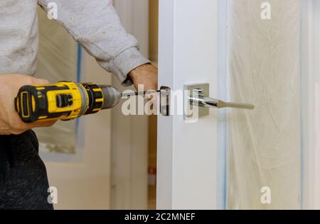 Manuale con un trapano a cacciavite per installare la serratura nella porta in una casa Foto Stock