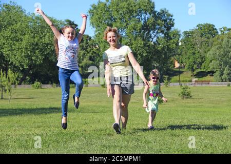 Madre felice che si diverte a saltare con le sue figlie su erba verde. Buon team di famiglia Foto Stock