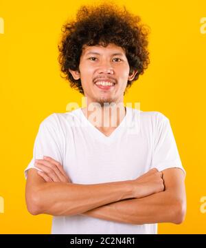 Ritratto di bell'uomo asiatico con capelli ricci con braccia incrociate isolato su sfondo giallo Foto Stock