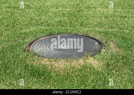 Tombino di metallo in uno sfondo di erba verde sul campo Foto Stock