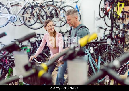 Venditore che aiuta la donna cliente in negozio di biciclette a trovare la bicicletta giusta Foto Stock