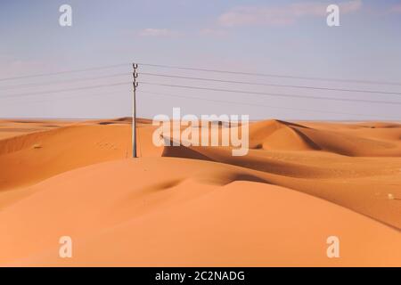 Splendido deserto di dune di sabbia rossastre con linee elettriche e pali di servizio all'orizzonte in Arabia Saudita Foto Stock