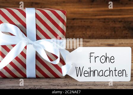 Un regalo di Natale con etichetta con la calligrafia tedesca Frohe Weihnachten significa buon Natale. La carta di avvolgimento di un arco Foto Stock