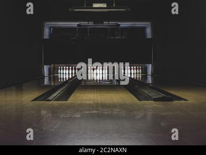 Concetto di svago, intrattenimento e attività. Sfondo astratto con spazio di copia di pista da bowling in parquet vecchio e scuro con spille bianche alla fine di Foto Stock