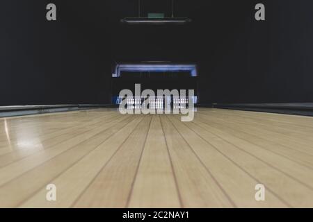 Concetto di svago, intrattenimento e attività. Sfondo astratto con spazio di copia di pista da bowling in parquet vecchio e scuro con spille bianche alla fine di Foto Stock