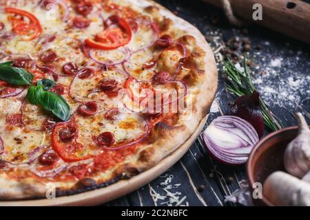 Pizza con salsicce, prosciutto, le cipolle e i pomodori. Concetto il volantino promozionale. Pizza su sfondo nero Foto Stock