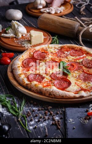 Composizione di salsiccia pizza e gli ingredienti per la sua preparazione. Sfondo pronto per il tuo design. Pizza su sfondo nero Foto Stock