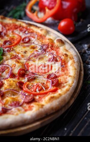 Pizza con salsicce, prosciutto, le cipolle e i pomodori. Poster per ristoranti o pizzerie. Pizza su sfondo nero Foto Stock