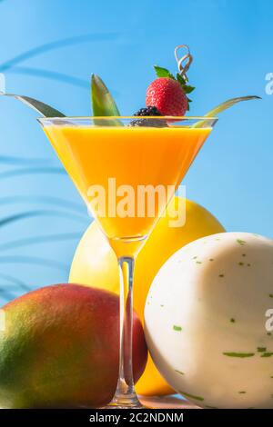 Primo piano di un appetitoso bicchiere di succo d'arancia martini con foglie e uno spiedino con una mora e una fragola, con un mango, un melone globo miele Foto Stock