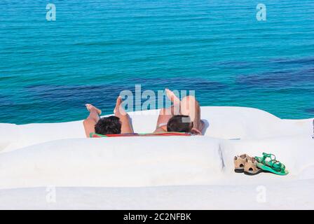 Due turisti su una spiaggia rocciosa bianca della Sicilia con il mare da acqua di colore verde-blu Foto Stock