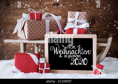 Lavagna con il tedesco Calligraphy Frohe Weihnachten und Ein Glueckliches mezzi 2020 Buon Natale e un felice 2020. La slitta con un regalo di Natale e Pr Foto Stock
