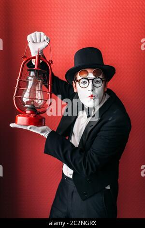 La pantomima attore di eseguire con la lanterna di kerosene. Commedia artista mime in tuta, guanti, occhiali, make-up maschera e cappello. Comico persona di sesso maschile con vintage Foto Stock