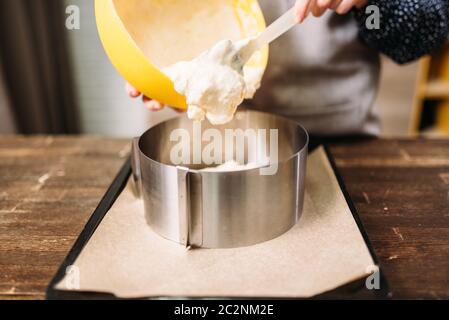 Donna cucinare in grembiule aggiunge la crema per la torta nella teglia. Cucina sullo sfondo Foto Stock