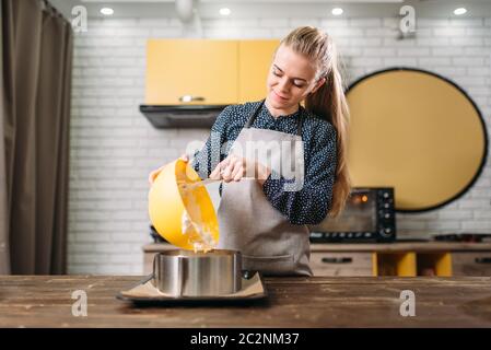 Donna cucinare in grembiule aggiunge la crema per la torta nella teglia. Cucina sullo sfondo Foto Stock