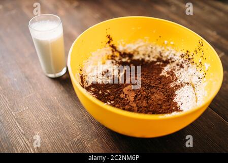 Ciotola con la pasta, il cioccolato in polvere e il bicchiere di latte su sfondo di legno. Torta dolce la cottura. Dessert fatti in casa ingredienti Foto Stock