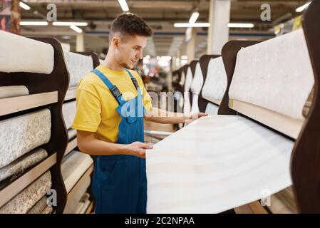 Costruttore maschile scelta di sfondi in negozio hardware. Costruttore in uniforme guardare la merce in negozio fai da te Foto Stock