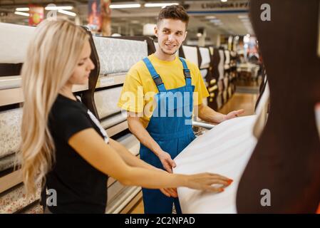 Assistente e cliente femminile che sceglie gli sfondi nel negozio di hardware. Venditore in uniforme e donna in negozio fai da te, shopping in costruzione supermercato Foto Stock