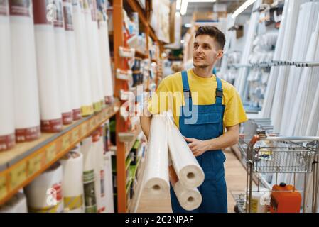 Costruttore maschile con rotolo di sfondi in negozio di hardware. Costruttore in uniforme guardare la merce in negozio fai da te Foto Stock