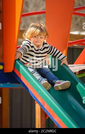 carina bambina che scivola giù per lo scivolo dei bambini Foto Stock