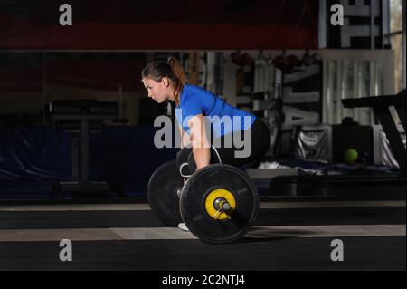 Giovane donna facendo allenamento deadlift con pesanti barbell in palestra scuro Foto Stock