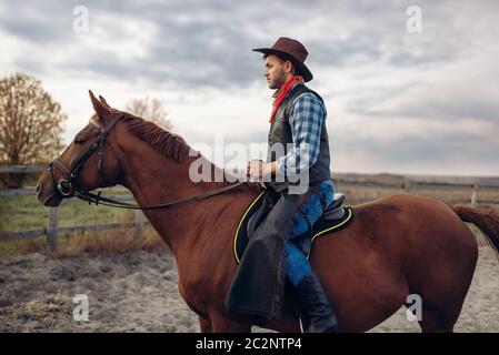 Cowboy in jeans e giacca di pelle in sella ad un cavallo sulla fattoria del Texas occidentale. Vintage persona di sesso maschile a cavallo, cultura americana Foto Stock