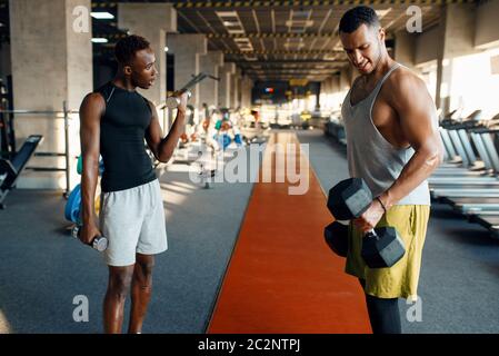 Due atleti stanchi che fanno esercizio con manubri, allenarsi in palestra. Allenamento in forma in club sportivo, stile di vita sano, fitness Foto Stock