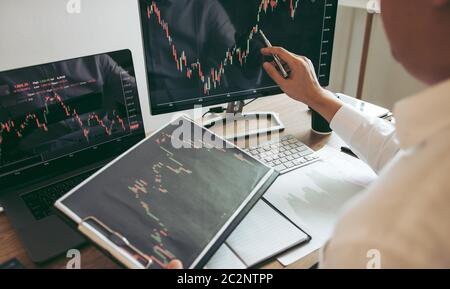 Investitore uomo che analizza il grafico del mercato azionario utilizzando una penna che punta allo schermo del computer. Foto Stock