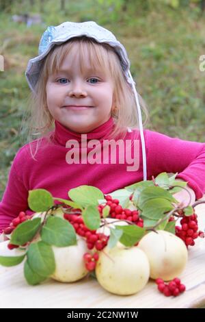 Ritratto di bambina con mele e schisandra. Gioiosa baby sorridendo vicino il raccolto di frutta Foto Stock