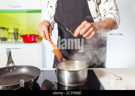 Uomo che aggiunge rosmarino alla carne sulla padella Foto Stock