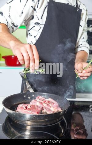 Uomo che aggiunge rosmarino alla carne sulla padella Foto Stock