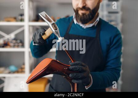 Calzolaio con martello chiodi le punte alla scarpa, servizio di riparazione calzature. Abilità artigiana, laboratorio di calzaturiera, lavori padronali con stivali, lavoro di acciottolato Foto Stock