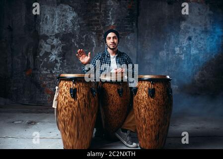 Batterista maschio giocando sul bongo in legno fusti nel negozio della fabbrica, musicista in movimento. Djembe, musicale strumento a percussione, ritmi etnici musica Foto Stock