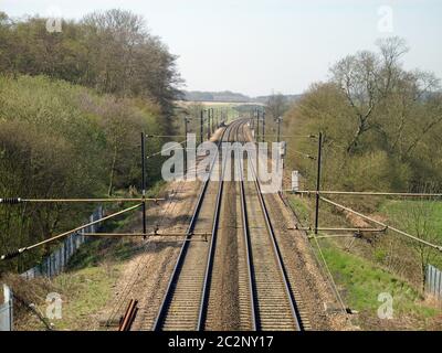 Immagine tratta da un ponte su una linea ferroviaria elettrica che mostra che la linea scompare in distanza e si incurva verso destra. Situato in un paesaggio rurale w Foto Stock