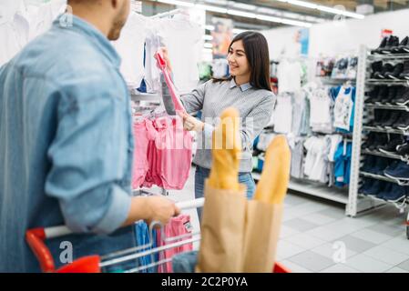 Giovane madre acquistare vestiti per bambini in negozio, famiglia shopping. I clienti in negozio, gli acquirenti nel mercato, dipartimento di beni per i bambini Foto Stock