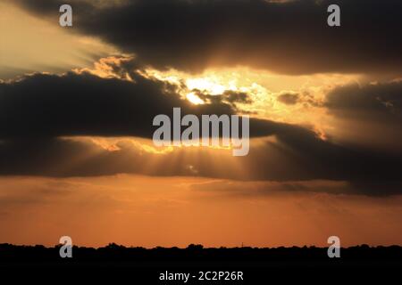 Tramonto colorato con nuvole e raggi solari che scendono dall'alto. Foto Stock