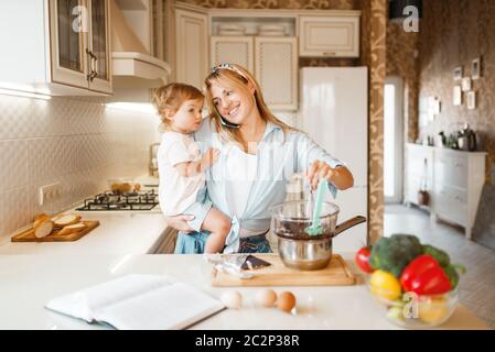 La giovane madre e la figlia preparano la pasta con cioccolato fuso. Carina donna e bambina che cucinano in cucina. La famiglia felice fa dolce desse Foto Stock