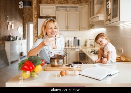 La giovane madre e sua figlia assaggia cioccolato fuso. Carina donna e bambina cucina, preparazione pasticceria. Happy Family prepara sw Foto Stock