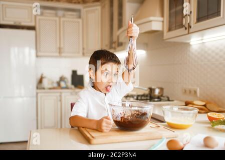 Bambino giovane che mescola il cioccolato fuso in una ciotola. Cucina carina ragazzo in cucina. Happy child prepara dessert dolci Foto Stock