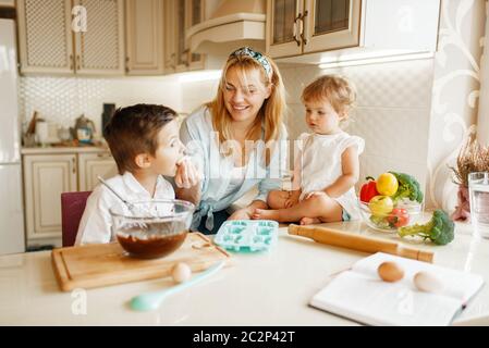 La giovane madre e i suoi figli gustano la pasta fresca con cioccolato fuso. Donna e bambini cucinano in cucina, preparazione di torte. Buona famiglia Foto Stock