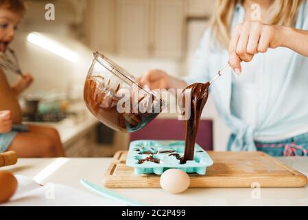 Giovane madre e bambino prepara la pasticceria e gusti cioccolato fuso. Carino donna e bambina cucina, preparazione torta. Felice famiglia ma Foto Stock