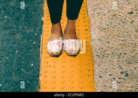 Donna che indossa scarpe da bambola in piedi su una linea gialla che mostra il concetto di allontanamento sociale, isolamento, il nuovo stile di vita normale e di viaggio durante la COV Foto Stock