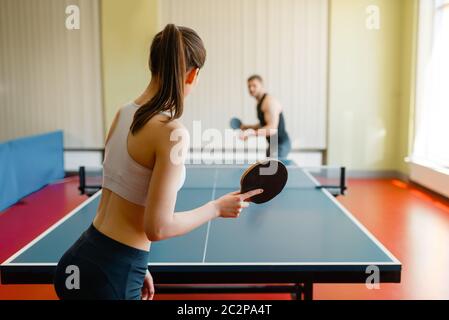 L uomo e la donna a giocare a ping pong all'interno. Matura in sportswear trattiene le racchette e gioca a tennis da tavolo in palestra Foto Stock