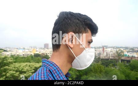Vista laterale dell'uomo che indossa la maschera facciale sullo sfondo della città. Foto Stock