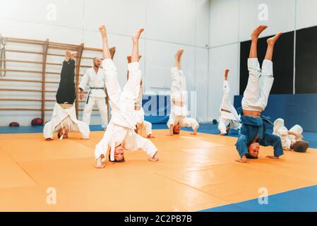 Bambini karate, kids in kimono pratica delle arti marziali di hall. Bambini e bambine in uniforme su sport training, capovolto esercizio Foto Stock