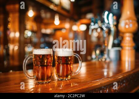 Due boccali da birra sulla barra di legno contatore, macro, nessuno. Oktoberfest simbolo o concetto. Occhiali con bevanda dorata e schiuma sul tavolo in pub, primo piano Foto Stock