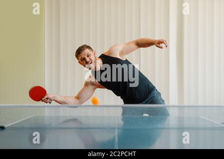 L'uomo con racchetta da ping pong gioca la palla fuori, immagine in azione, allenamento in interni. Uomo in abbigliamento sportivo, allenamento in ping-pong club Foto Stock