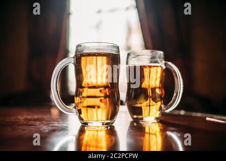 Due boccali da birra sulla barra di legno contatore, vista macro, nessuno. Oktoberfest simbolo. Occhiali con bevanda dorata sulla tavola in pub, closeup, finestra con su Foto Stock